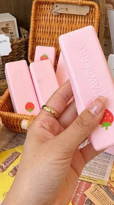 Hand holding a pink soap bar with strawberry design in a store setting
