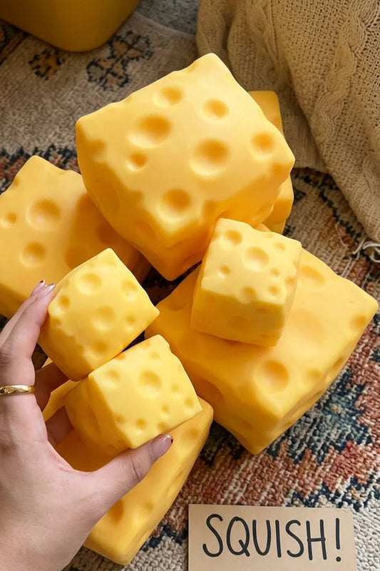 Yellow cheese-shaped sponges with a hand holding one, on a patterned rug with 'Squish! 